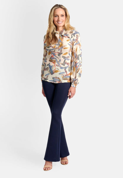 Model wearing creme silk high neck long sleeve blouse top printed with feathers and stretch knit navy pants