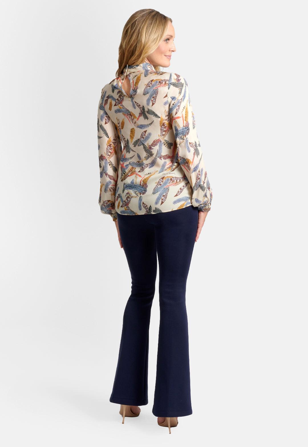 Model wearing creme silk high neck long sleeve blouse top printed with feathers and stretch knit navy pants