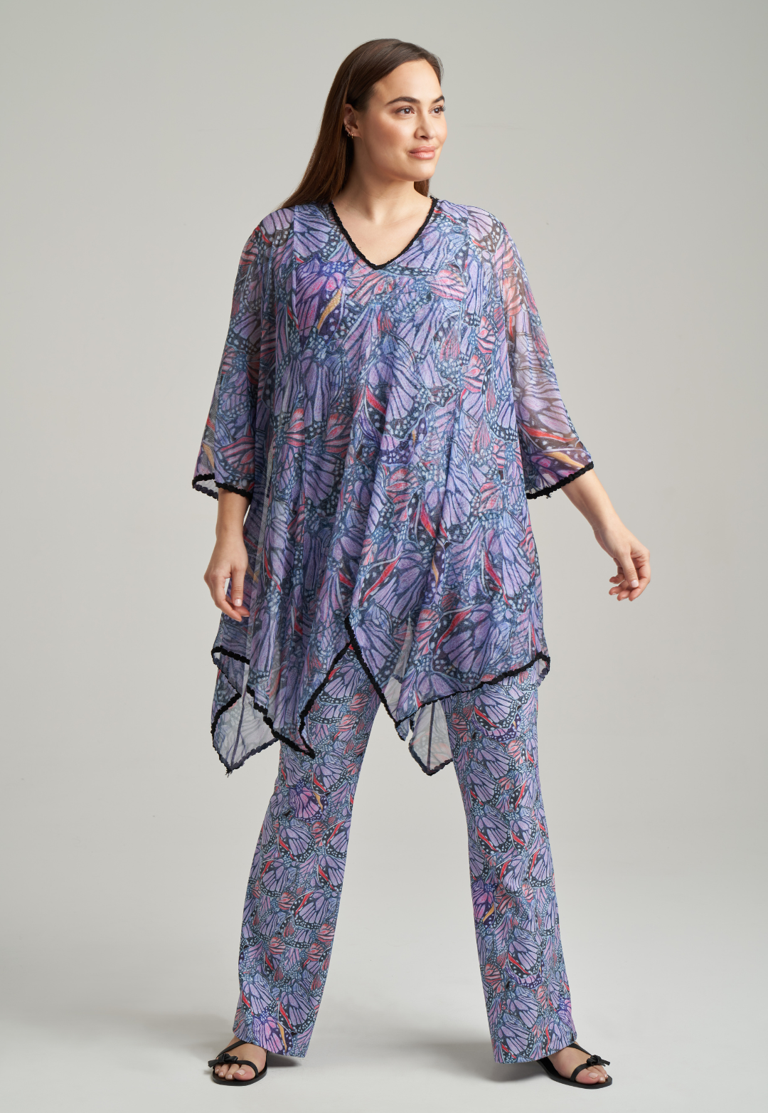Woman wearing butterfly printed mesh poncho with black trim over printed stretch knit tank top and stretch knit pants by Ala von Auersperg for spring summer 2021