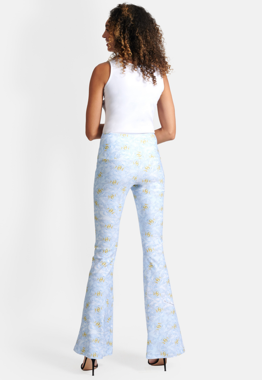 Woman wearing blue and yellow feather printed stretch knit pants with white stretch knit tank top by Ala von Auersperg